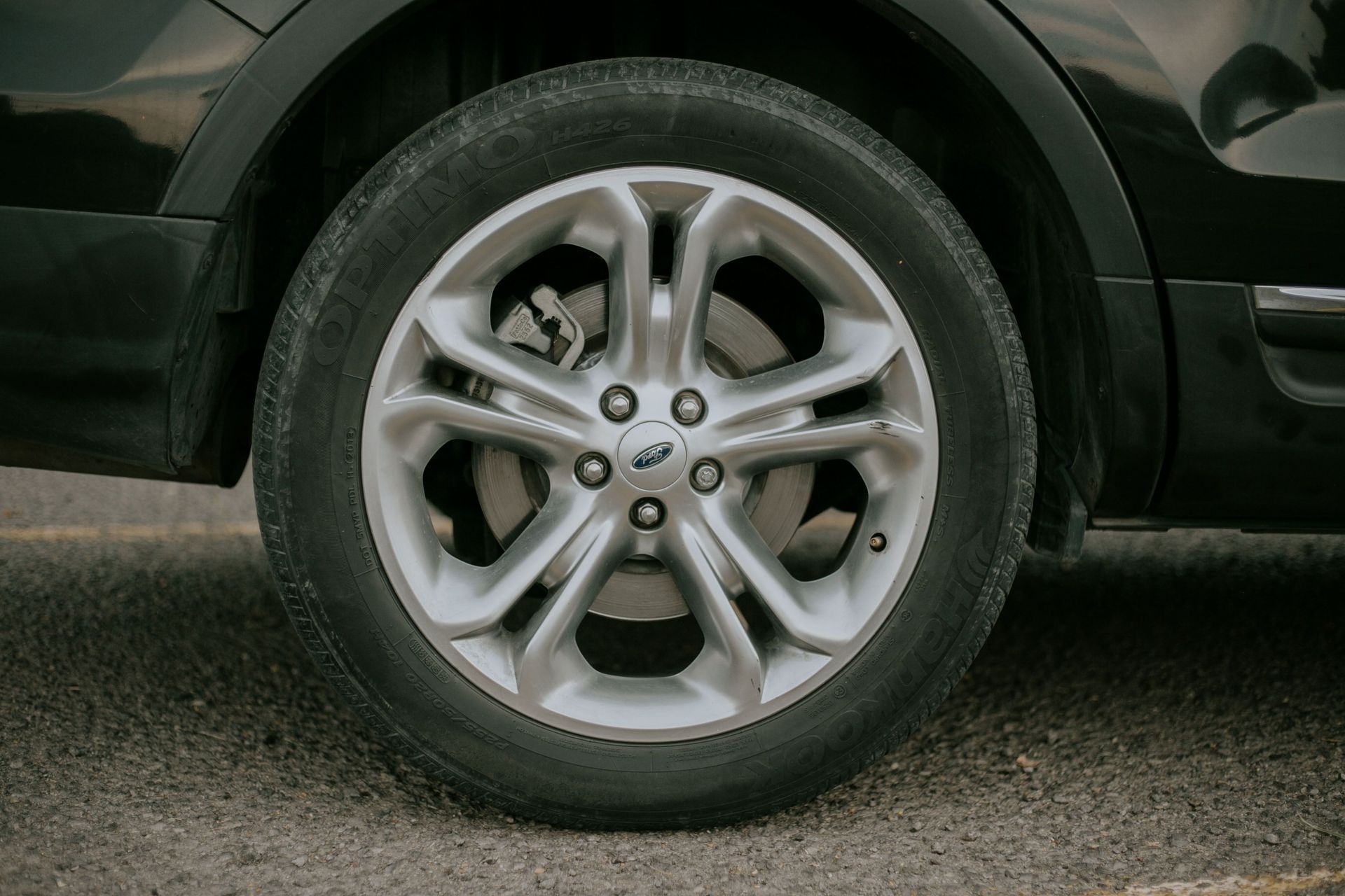 Detailed close-up of a car tire with an alloy rim parked on asphalt.