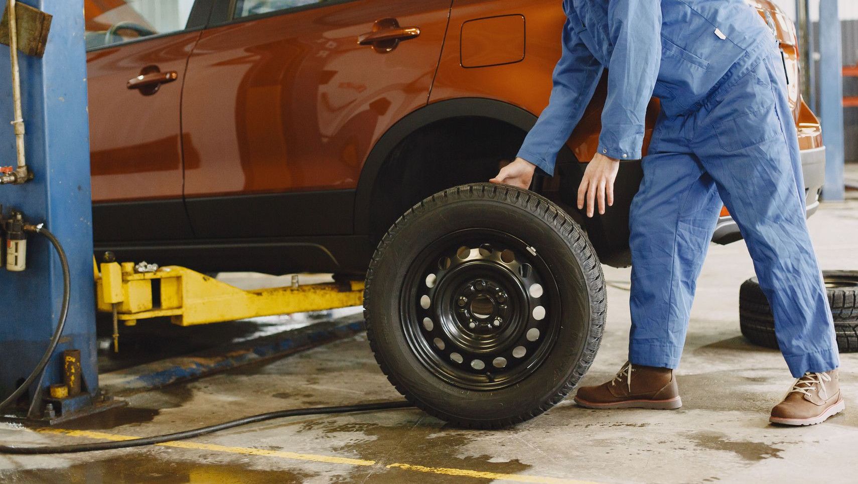 Mechanic in blue coveralls replacing tire on red SUV in repair shop garage.